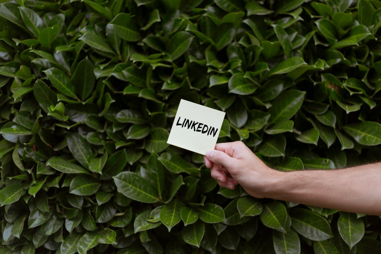 A hand holds a LinkedIn note against a lush green leaf background.